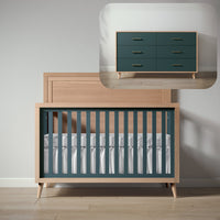 Wooden crib with green and white bedding next to a matching dresser in a minimalistic room.