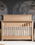 Nursery with wooden crib, gray bedding, and moon-themed wall decor.